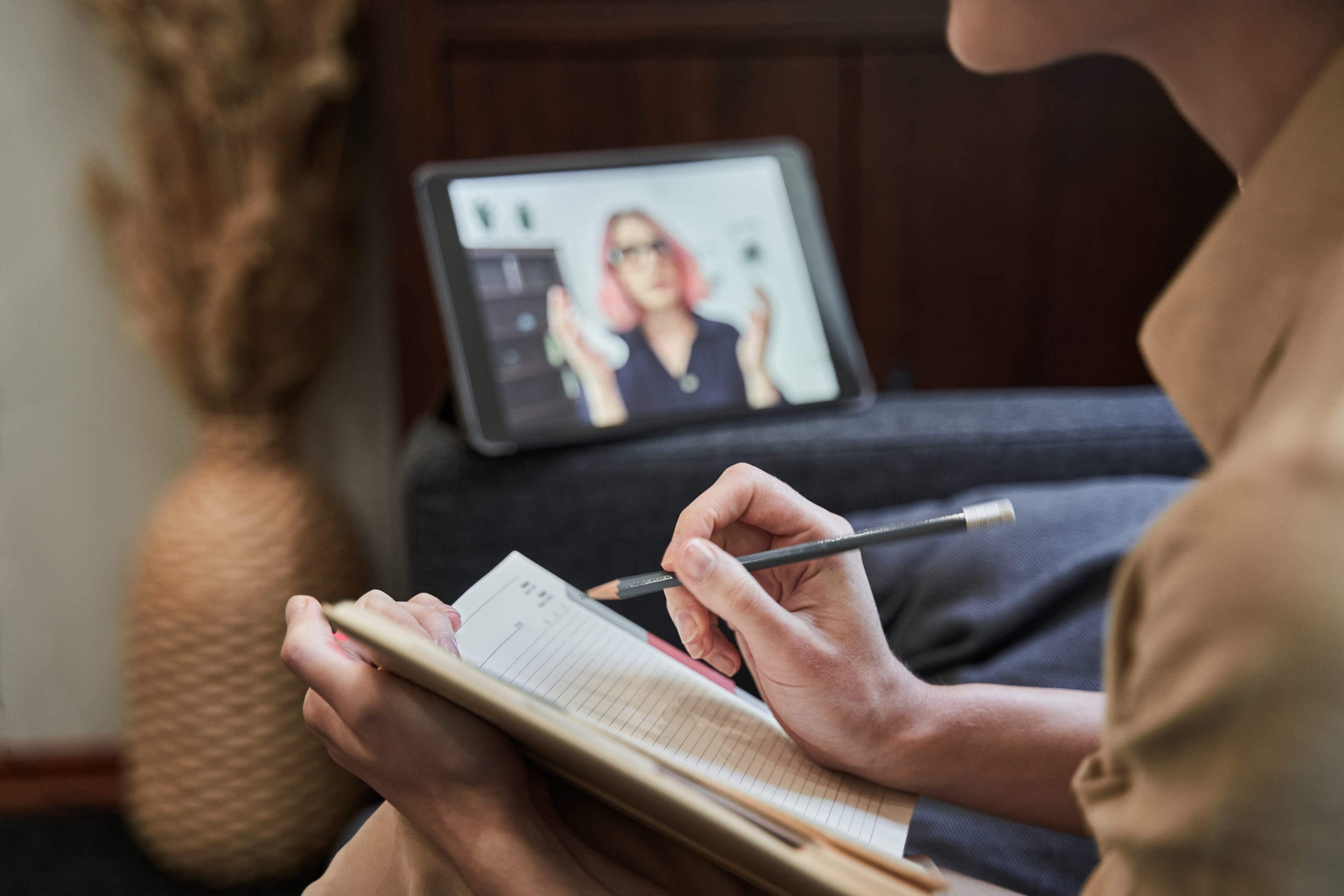 Cropped view of young female psychotherapist is holding a notebook and making notes during the online session while sitting in office. Stock photo